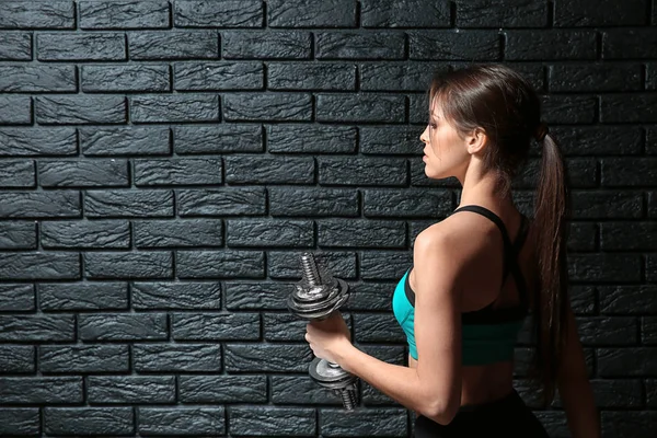 Karanlık tuğla duvar yakınındaki dumbbells ile sportif genç kadın