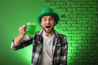 Yakışıklı genç adam yeşil şapkalı ve renk arka plan üzerinde bira kupa ile. Aziz Patrick günü kutlama