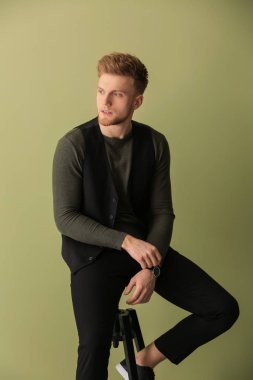 Dışkı rengi arka plan üzerinde oturan moda genç adam