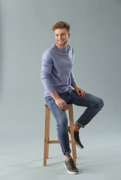 Fashionable young man sitting on stool against grey background