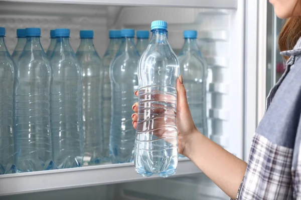 Bir kadın dükkandaki buzdolabından su alıyor.