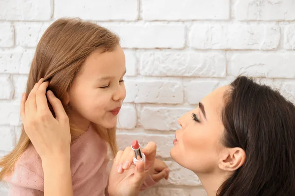 Young Mother Applying Lipstick Daughter Lips White Brick Background — Stock Photo, Image