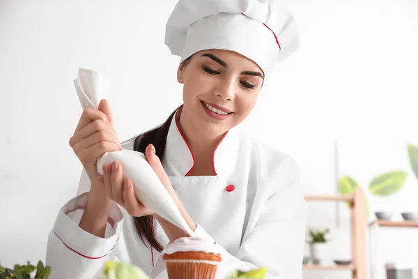 Young female confectioner decorating cupcake in kitchen