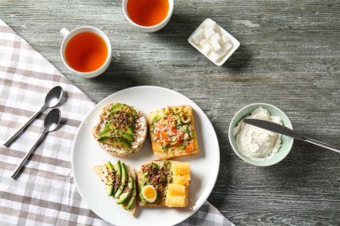 Plaka farklı lezzetli sandviçler ve ahşap masa üzerinde çay