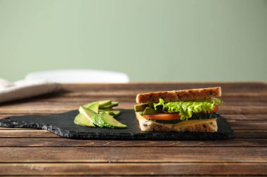 Lezzetli sandviç ve ahşap masa üzerinde avokado ile kayrak plaka