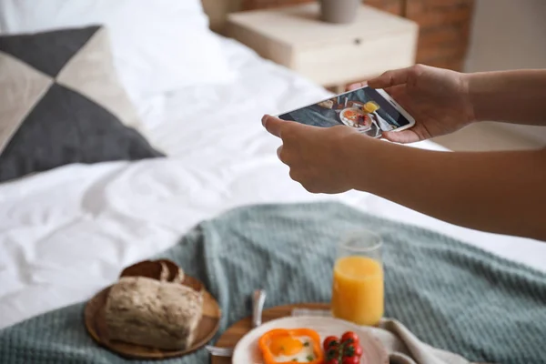 Female food photographer with mobile phone taking picture of tasty breakfast at home, closeup