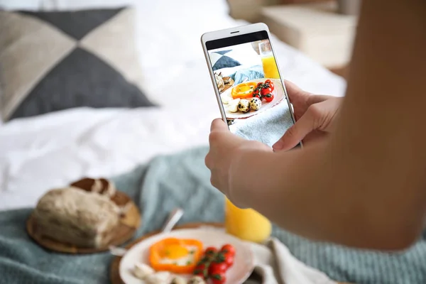 Female food photographer with mobile phone taking picture of tasty breakfast at home, closeup