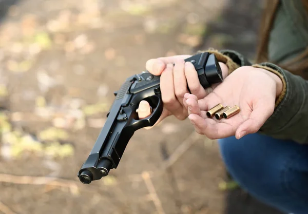 Young depressed woman with gun and bullets thinking about suicide outdoors