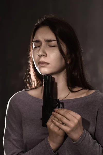 Young woman with gun is going to commit suicide on dark background