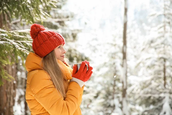 Beautiful woman with hot drink in winter forest