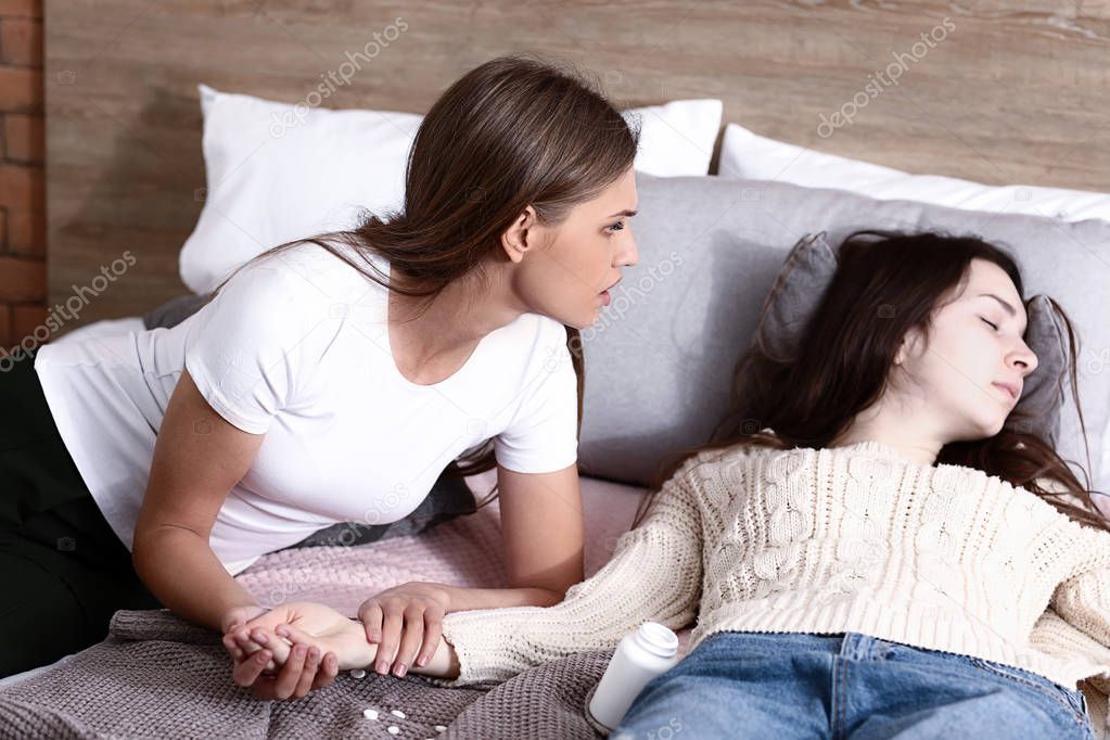 Young afraid woman measuring pulse of her unconscious friend. Suicide concept