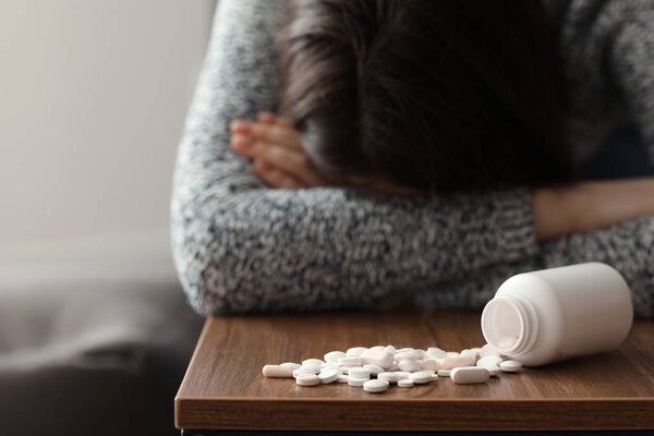 Depressed woman near heap of pills on table at home