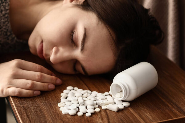 Young unconscious woman with pills on table. Suicide concept