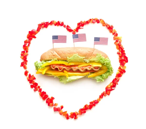 Tasty hot dog with USA flags in heart-shaped frame on white background