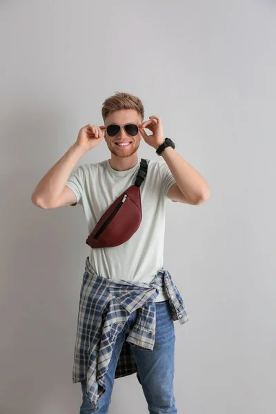 Fashionable young man with bag on light background