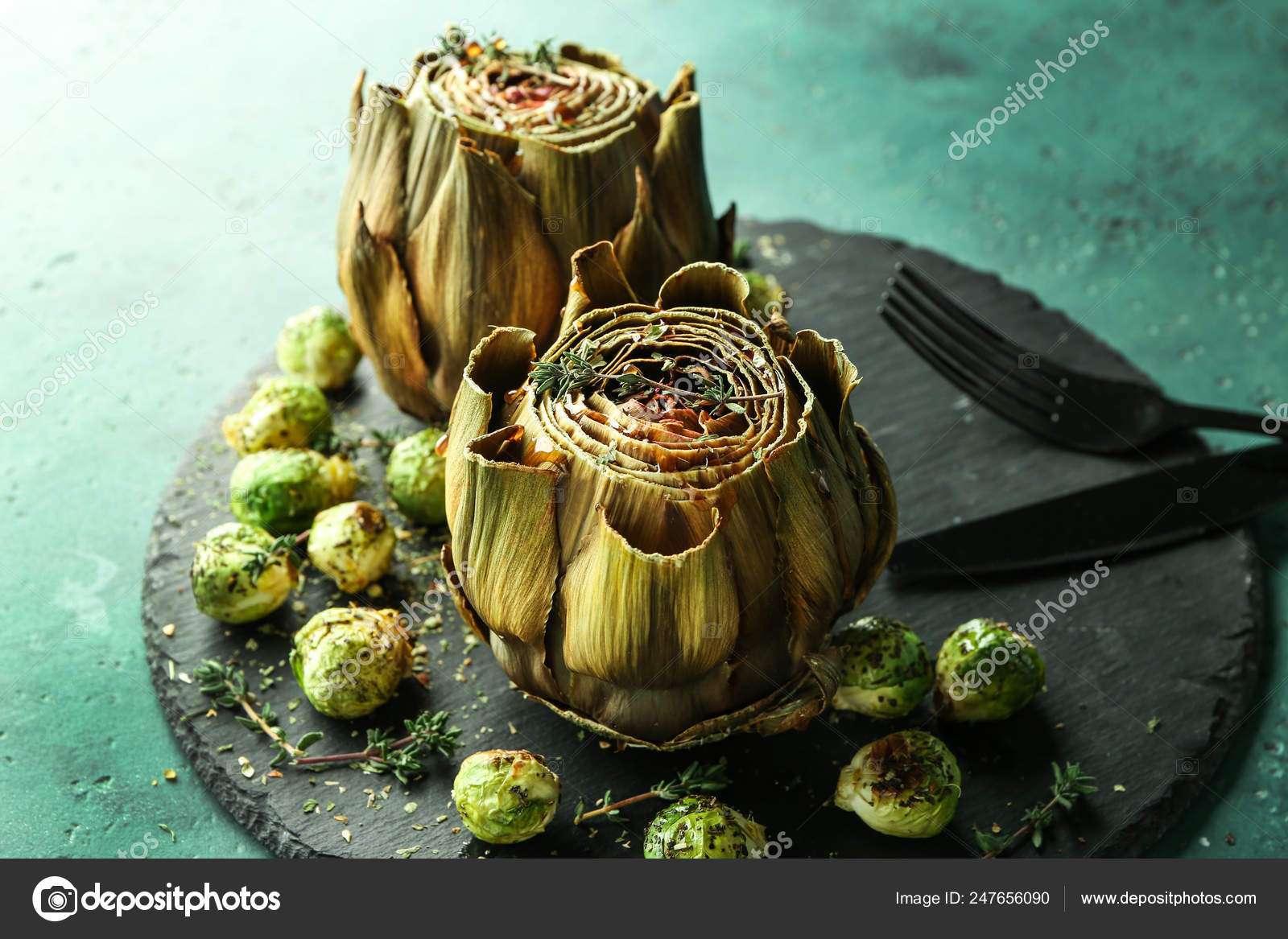 Slate plate with tasty baked artichokes and Brussels sprouts on table