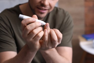 Diyabetli adam evde tükenmez kalemle kan örneği alıyor.