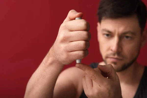 Diabetiker man tar blodprov med lansetten penna på färg bakgrunden — Stockfoto