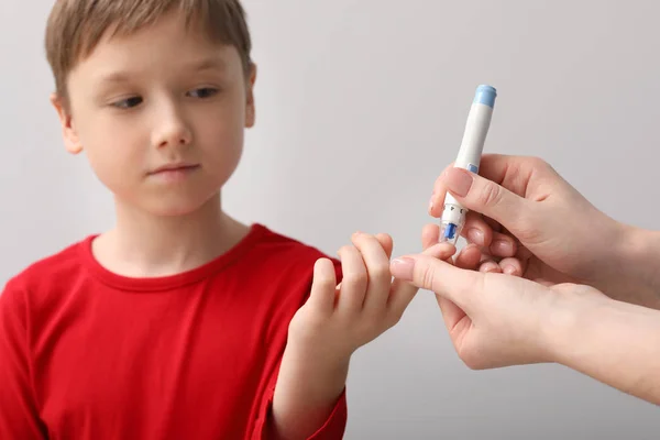 Mother taking blood sample of her diabetic child with lancet pen on light background