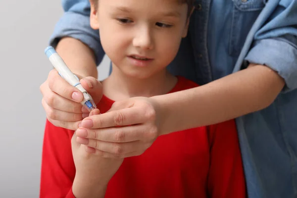 Mor att ta blodprov på hennes diabetes barn med lansetten penna — Stockfoto