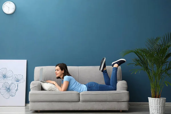 Beautiful young woman with laptop lying on sofa at home — Stock Photo, Image