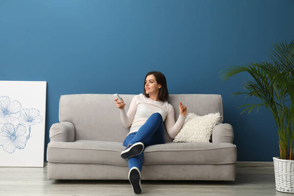 Young woman switching on air conditioner at home