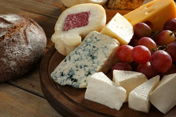 Wooden board with assortment of tasty cheese and bread on table — Stock Photo, Image