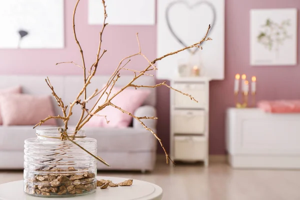 Vase with golden nuggets and tree branches on table in room