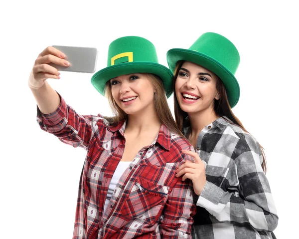 Lindas mulheres jovens em chapéus verdes tomando selfie no fundo branco. Celebração do Dia de São Patrício — Fotografia de Stock