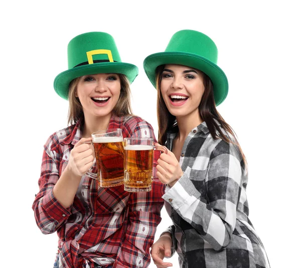 Jovens mulheres bonitas com chapéus verdes e canecas de cerveja no fundo branco. Celebração do Dia de São Patrício — Fotografia de Stock