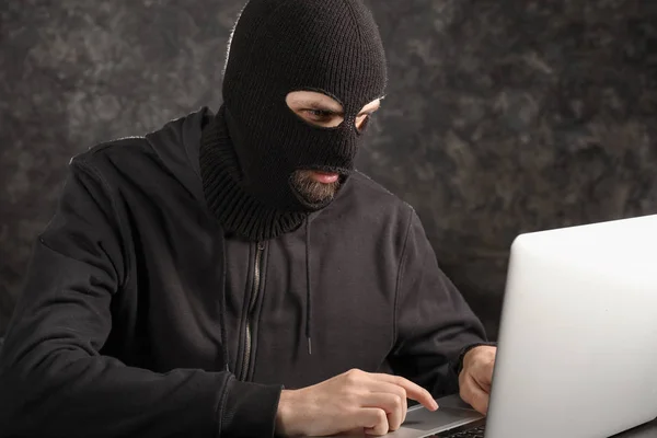 Maschio hacker in maschera utilizzando computer portatile su sfondo scuro — Foto Stock