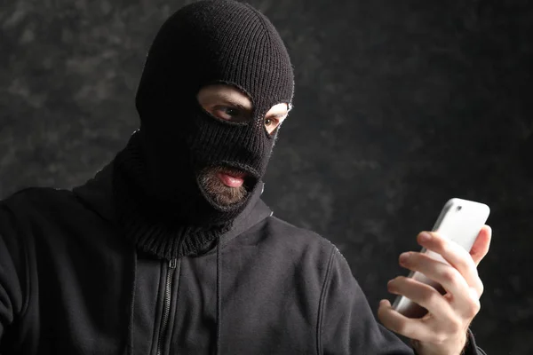 Mężczyzna hacker w masce i z telefonu komórkowego na ciemnym tle — Zdjęcie stockowe