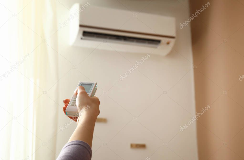 Young woman switching on air conditioner at home
