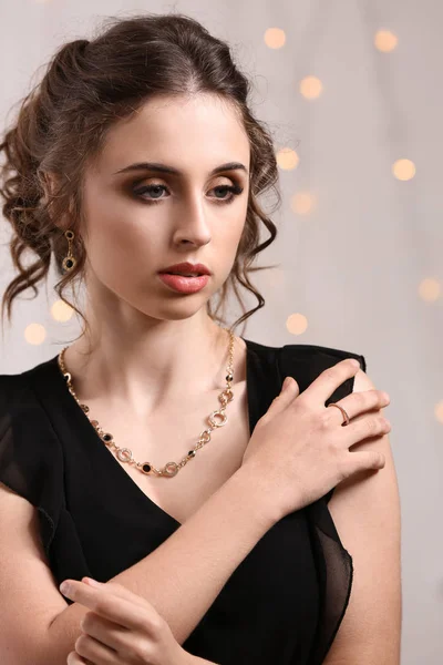 Ung kvinna med vackra smycken mot oskärpa lampor — Stockfoto