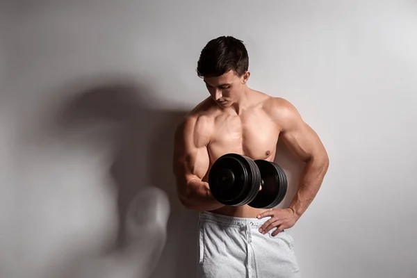 Muskulöser Bodybuilder mit Hantel auf hellem Hintergrund — Stockfoto