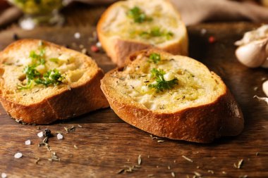 Ahşap masanın üzerine zeytinyağı, sarımsak ve otlar ile ekmek dilimlenmiş