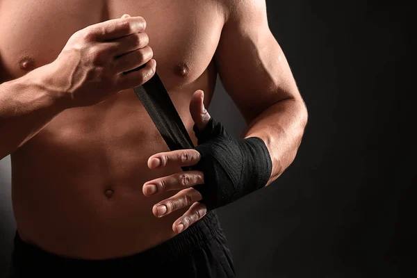 Attractive sportsman winding wrist band against dark background — Stock Photo, Image