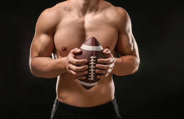 Muscular fisiculturista com bola de rugby no fundo escuro — Fotografia de Stock