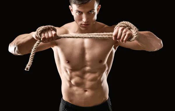 Muskulös bodybuilder med rep på mörk bakgrund — Stockfoto