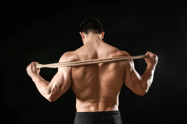 Muscular bodybuilder with rope on dark background, back view — Stock Photo, Image