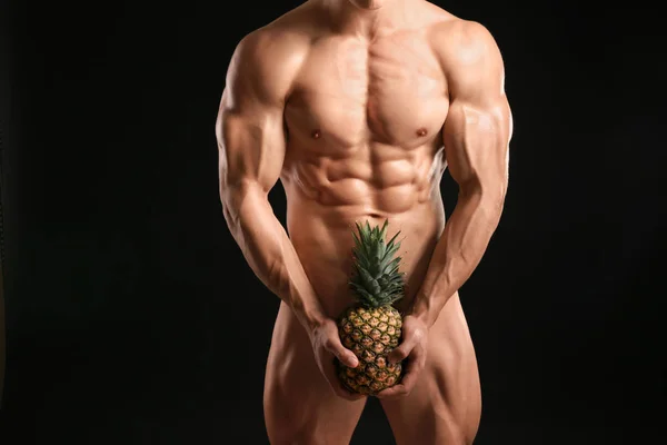 Muscular sexy bodybuilder with pineapple on dark background — Stock Photo, Image