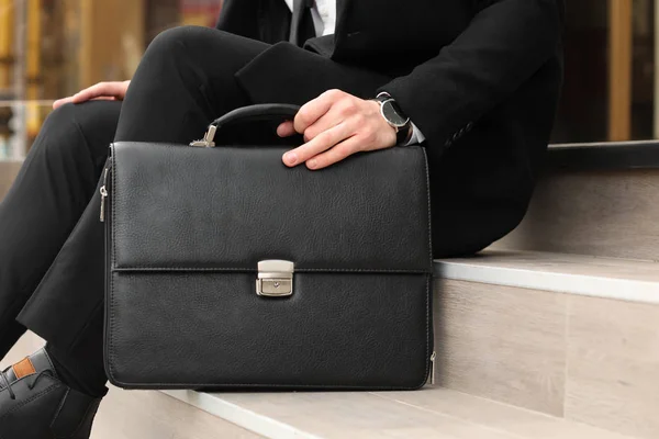 Businessman with stylish briefcase sitting on stairs outdoors