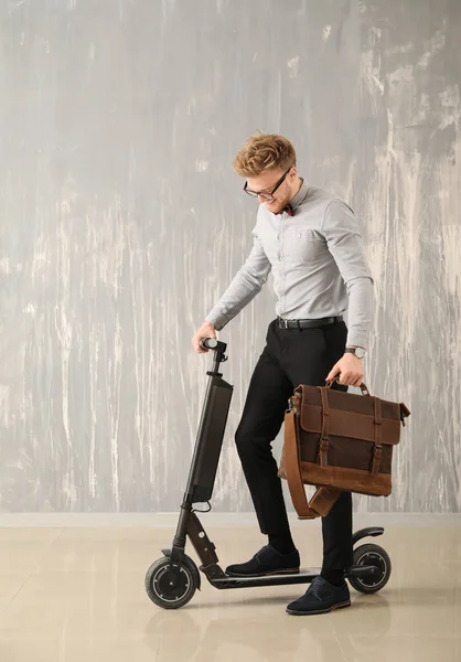 Hombre de negocios guapo con elegante maletín y scooter cerca de la pared gris — Foto de Stock