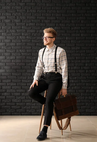 Handsome businessman with stylish briefcase near dark brick wall