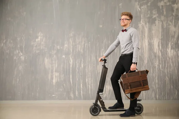 Hombre de negocios guapo con elegante maletín y scooter cerca de la pared gris — Foto de Stock