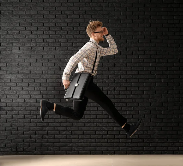 Jumping businessman with stylish briefcase on dark brick background — Stock Photo, Image