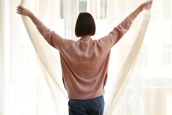 Jonge vrouw opent gordijnen in de ochtend — Stockfoto