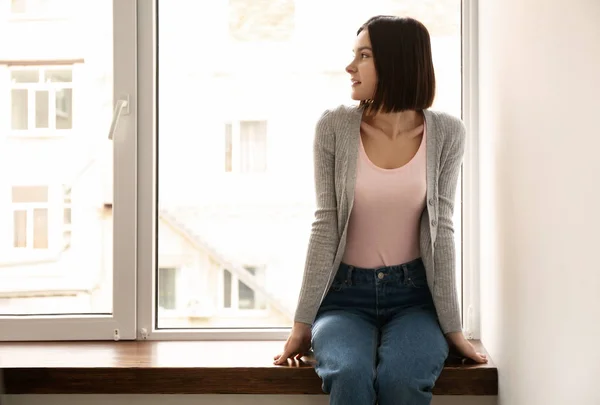 Young woman sitting on window sill at home — Stock Photo, Image