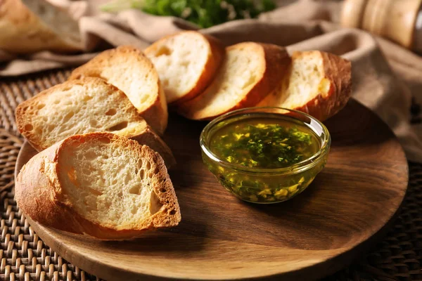 Sliced bread and bowl with olive oil, garlic and herbs on wooden plate — Stock Photo, Image