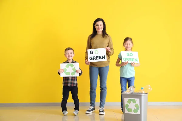 Família segurando folhas de papel com texto GO VERDE e símbolo de reciclagem perto da parede de cores — Fotografia de Stock